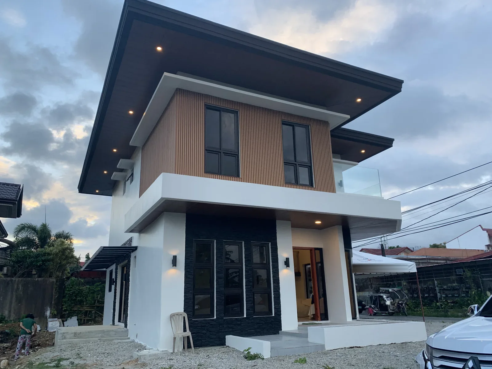 Two-storey house at dusk with a timber-clad upper floor, a black stone ground floor and a deep roof overhang