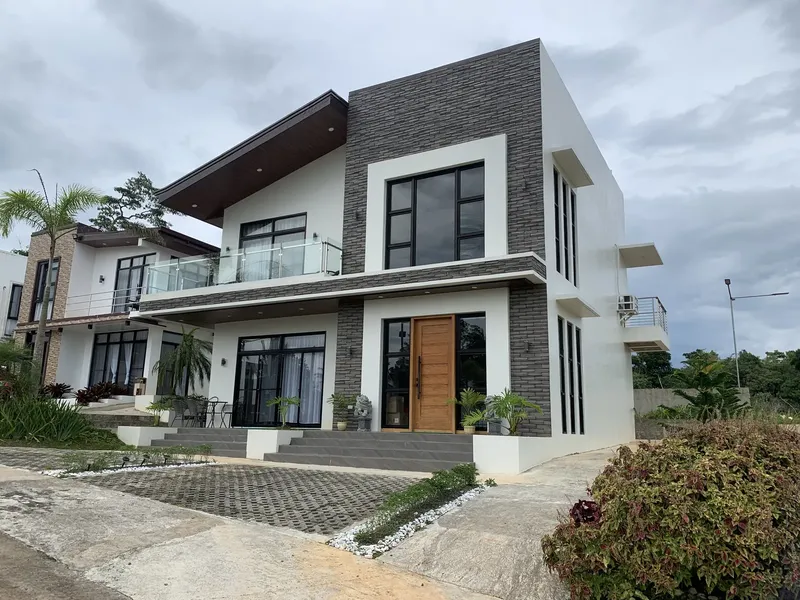 Two-storey house with dark stone cladding, a glass balcony and a timber door