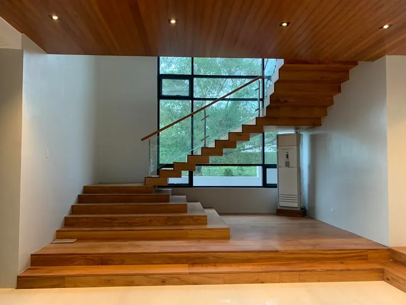 Open timber staircase rising from a double-height hall with large windows